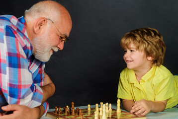 Grandfather and grandson spend time together playing chess at home. Grandpa teaching grandchild to...