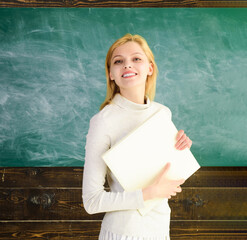Back to school. Portrait of smiling female student girl with book near blackboard in university....