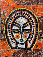 Colorful mosaic of a stylized ethnic face.Abstract mosaic wall art decoration.Close-up detail of a public art mosaic panel.Ancient-style ornamental face created with the trencadis mosaic technique