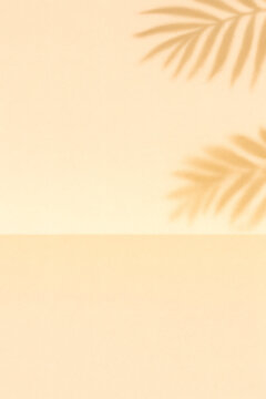 Tranquil tropical background with palm leaves casting shadows on a neutral tan colored two-tone surface creating a calm and relaxing scene.