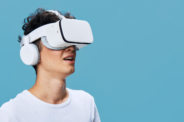 young man wearing virtual reality headset and headphones enjoying immersive experience with blue background in casual white t-shirt technology concept