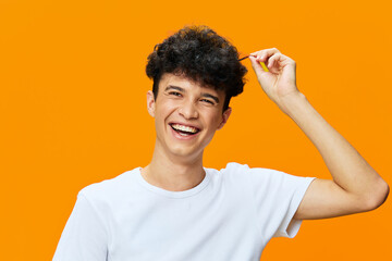 smiling young man with curly hair wearing white t-shirt on vibrant orange background, happy...