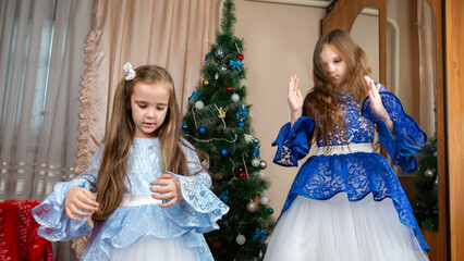 Little girls in festive dress dancing near christmas tree at home