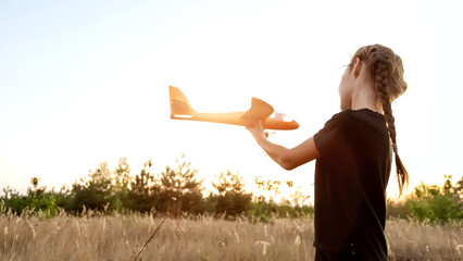 Girl play with toy airplane. Children toy plane in hands of child in summer in park under sun. Concept of child's dream of flying, child runs across field at sunset.