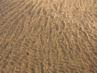 The image is of a sandy beach with ripples in the sand. The ripples are caused by the waves of the...