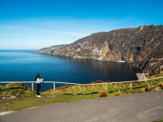 Teenager girl sightseeing stunning Slieve League cliff nature scenery and Atlantic ocean. Blue...