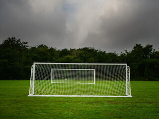 Clean cut football or soccer training ground with two goal posts, dark trees and dramatic sky in the background. Popular world sport. Team development area. Nobody.