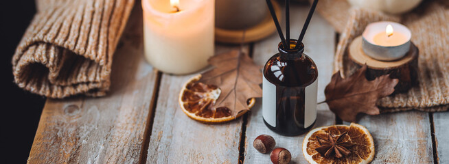 Home comfort, coziness, aromatherapy. Cozy interior with knitting, burning candles and aroma perfume diffuser in the living room. Fall scent, sweet pumpkin pie fragrance dry leaves, autumn mood banner