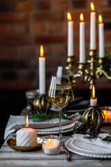 Beautiful table setting for family Christmas dinner at home. Cozy atmosphere, candlelight. Wine glasses, vintage chandelier, elegant interior. Fir tree branches, wooden furniture, dark, bokeh