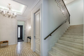 A hall with an entrance door and a staircase in a mansion decorated in neoclassical style. 
A...
