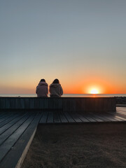 Two women sitting on a bench watching the Sunrise by the Lake Michigan, golden hour, Chicago, Illinois, USA