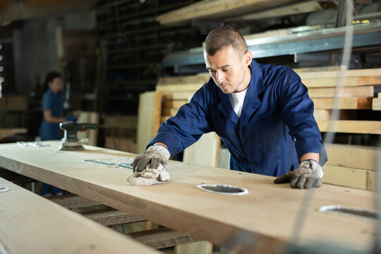 Young man worker wipes oak plank with rag in oak workshop