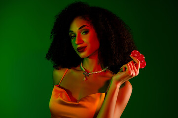 Elegant young woman with luxurious style holding poker chips in vibrant green lighting