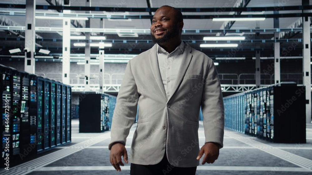 Poster smiling employee walking in high tech data center with machines powering networks, running companies