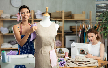 Woman tailor connects parts of dress on mannequin. Female craftsman attaches front part of dress to...