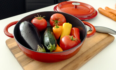 red beautiful cast iron skillet and fresh vegetables. cooking vegetable stew in cast iron. fresh...