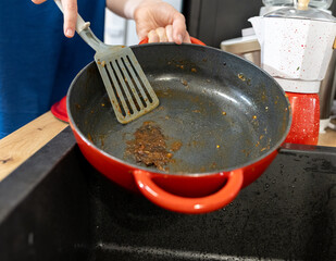 man in kitchen trying to clean food burnt to cast iron pan, hand washing cast iron cookware