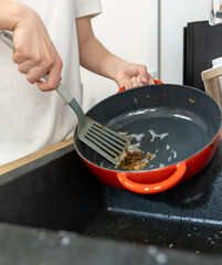man in kitchen trying to clean food burnt to cast iron pan, hand washing cast iron cookware