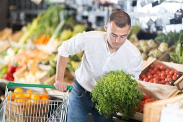 In vegetable department of bio supermarket, male customer took crisp lettuce from window. Man buys...