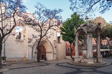 Beautiful view of the Carmo Convent ruins and ornate stone fountain in a tranquil Lisbon square,...