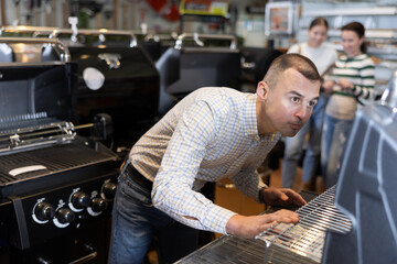 Young man buyer chooses bbq grill in hardware store