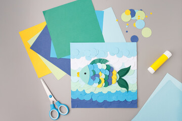 Paper sea scene with colorful fish and waves built from cut circles, framed by glue and scissors,...