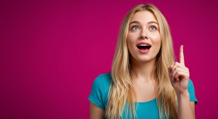 Obraz premium Portrait of a blonde woman in blue shirt pointing upwards with a pink colored background