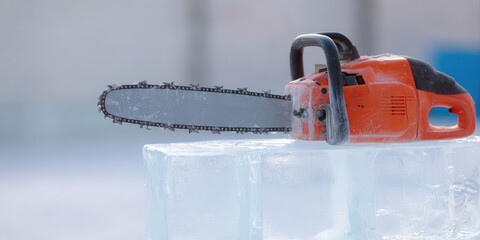 Naklejka premium A chainsaw is resting on top of a large block of ice in a stationary position. Concept: tools and equipment, ice sculpting, winter work