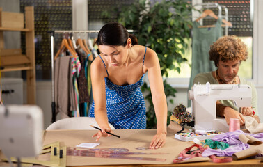 Woman tailor draw dress pattern of product on paper using curve ruler. Man craftsman tailor work...