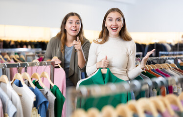 Enthusiastic young girls pointing each other to new clothes in the mall