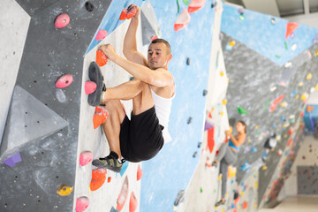 Active young man engaged in bouldering activity in rock climbing hangar
