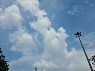 floodlight pole in a parking area with sky and leafy trees in the background, used for outdoor...
