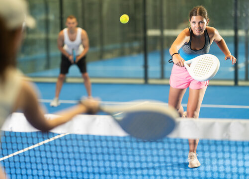 Young girl paired with a man plays padel on an indoor tennis court - Powered by Adobe
