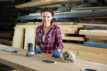 Adult female worker posing with oak plank at work in oak workshop