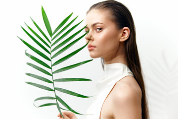 Elegant female model with palm leaf, showcasing natural beauty, serene expression, and minimalist...