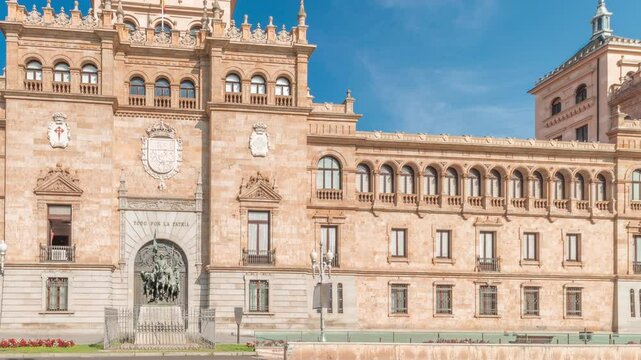 Panorama showing Cavalry Academy facade timelapse in Plaza de Zorrilla, Valladolid, Spain. Historic military building with intricate architecture, surrounded by busy urban scene under blue cloudy sky