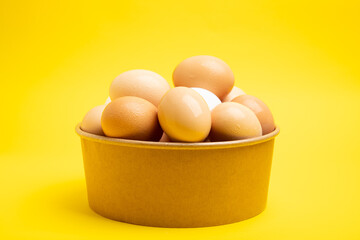 Brown eggs in paper bowl – front view, on yellow background