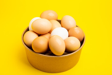 Brown and white eggs in paper bowl – top view, yellow background