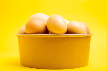 Brown eggs in paper bowl – front view,yellow background