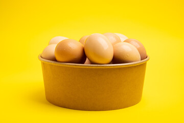 Brown eggs in paper bowl on yellow background