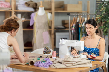 Female seamstress sewing on a sewing machine. Female tailor drawing dress sketches on paper