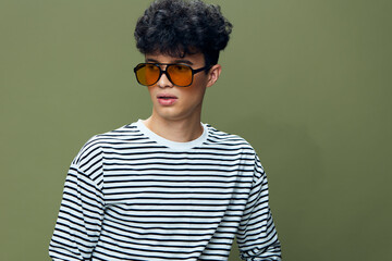 young man wearing striped shirt and orange sunglasses posing against green background with casual hairstyle and serious expression, studio portrait