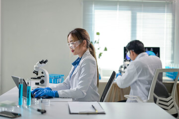 Scientist working with laptop in laboratory with microscope and test tubes