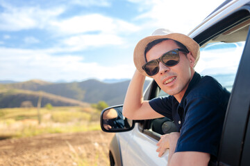 Happy traveler enjoying the breeze with his head out the car window during a road trip. Bright day,...