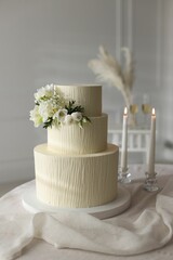 Delicious wedding cake with floral decor and burning candles on table indoors