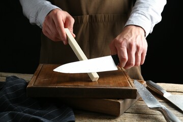 Man sharpening knife with sharpener on wooden table, closeup