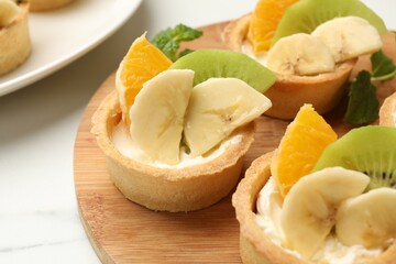 Tartlets with fruits and mint on white marble table, closeup. Delicious dessert