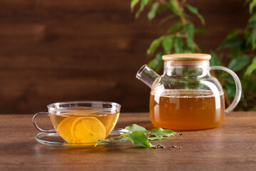 Cup of tasty green tea with lemon and teapot on wooden table
