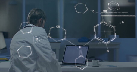 Studying lab coat scientist using laptop at bench with papers and chemical graphics, copy space