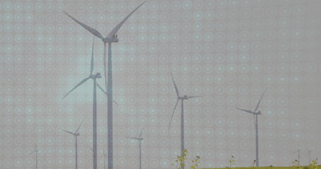 Spinning wind turbines generating electricity on grassy plain under overcast sky, with low shrubs